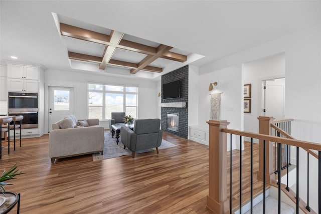 living room featuring coffered ceiling, a fireplace, beamed ceiling, and wood finished floors