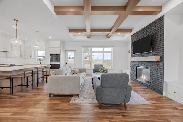 living area with light wood-type flooring, a brick fireplace, plenty of natural light, and coffered ceiling