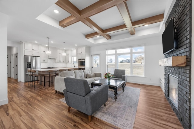 living room with baseboards, coffered ceiling, wood finished floors, a brick fireplace, and beam ceiling