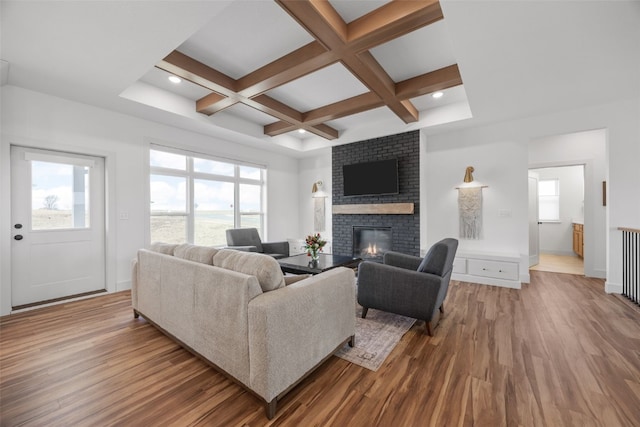 living room with coffered ceiling, a brick fireplace, wood finished floors, and beam ceiling