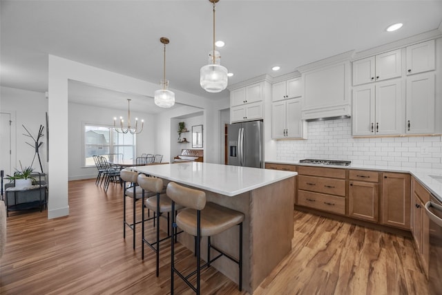 kitchen featuring decorative backsplash, a kitchen island, appliances with stainless steel finishes, light wood-type flooring, and a kitchen bar