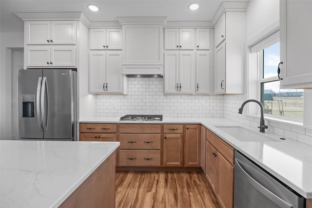 kitchen featuring stainless steel appliances, a sink, white cabinetry, backsplash, and light wood finished floors