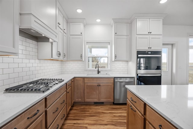 kitchen with white cabinets, light wood-style flooring, light stone counters, stainless steel appliances, and a sink