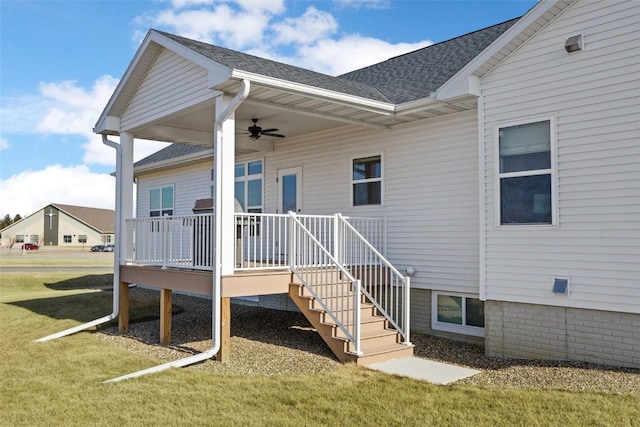 property entrance featuring a ceiling fan, a yard, a wooden deck, and a shingled roof