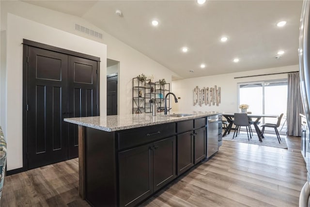 kitchen with a center island with sink, visible vents, a sink, vaulted ceiling, and stainless steel dishwasher