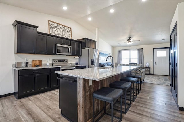 kitchen with a sink, stainless steel appliances, a kitchen bar, and light wood-style flooring