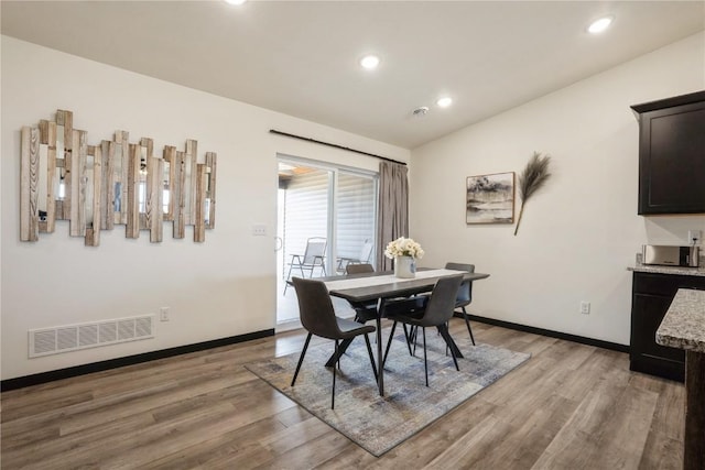 dining room featuring light wood-style flooring, visible vents, vaulted ceiling, and baseboards