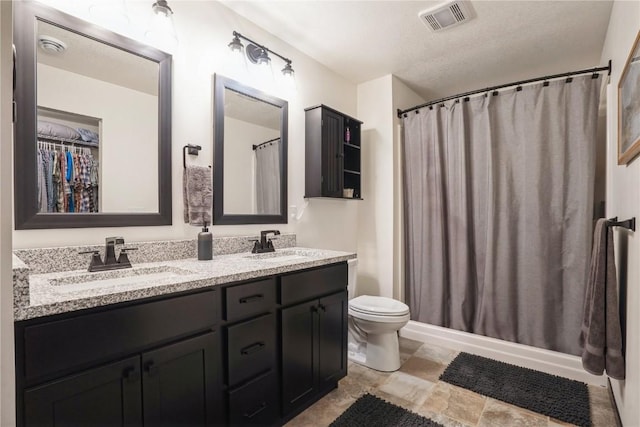 bathroom featuring toilet, double vanity, a sink, and visible vents