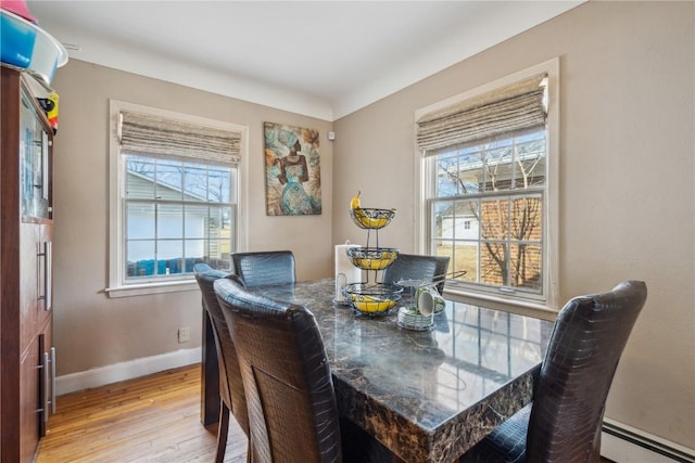 dining area featuring plenty of natural light, a baseboard heating unit, light wood-style flooring, and baseboards