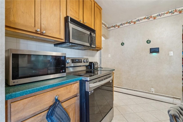 kitchen with light tile patterned floors, tasteful backsplash, appliances with stainless steel finishes, brown cabinetry, and a baseboard heating unit