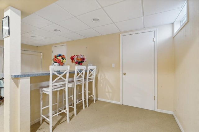 carpeted dining area featuring a paneled ceiling and baseboards