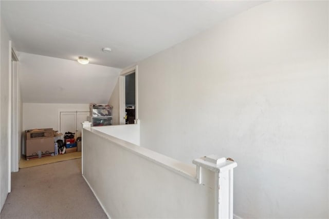 corridor with vaulted ceiling, an upstairs landing, and light colored carpet