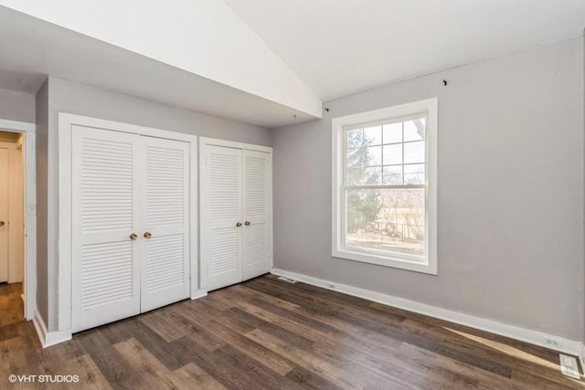 unfurnished bedroom with vaulted ceiling, dark wood-type flooring, multiple closets, and baseboards