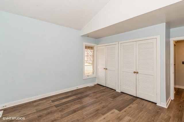 unfurnished bedroom with lofted ceiling, multiple closets, baseboards, and wood finished floors