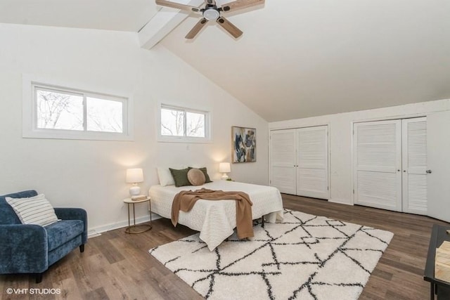 bedroom featuring baseboards, a ceiling fan, lofted ceiling with beams, wood finished floors, and two closets