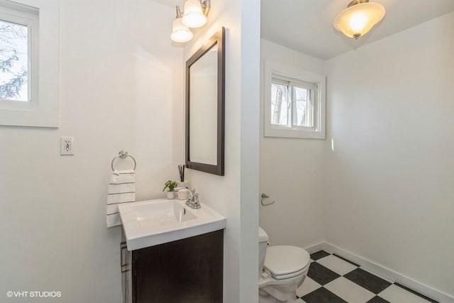 half bath with toilet, baseboards, vanity, and tile patterned floors