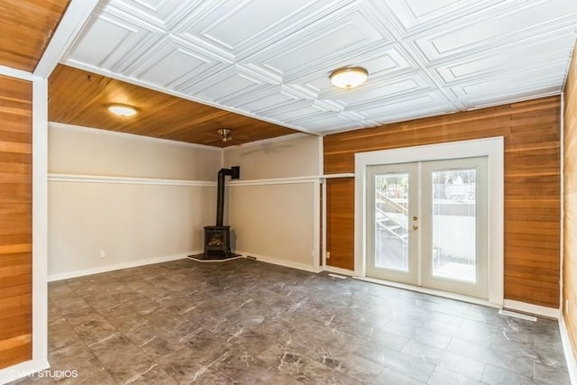 unfurnished living room with an ornate ceiling, wood walls, baseboards, french doors, and a wood stove