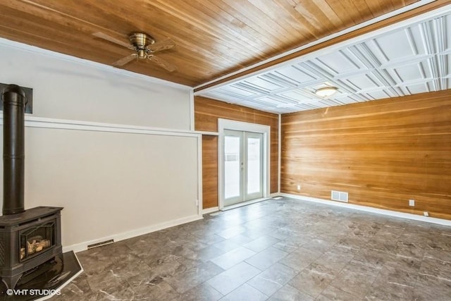 unfurnished living room featuring french doors, visible vents, a wood stove, wooden walls, and baseboards