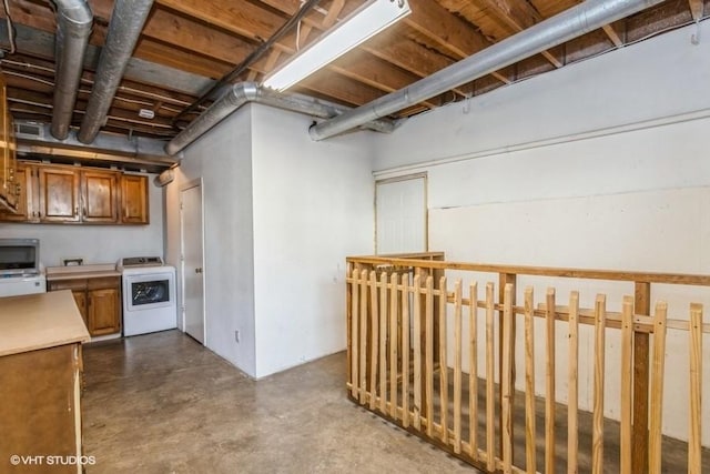 kitchen featuring washer / clothes dryer, light countertops, stainless steel microwave, brown cabinetry, and concrete floors