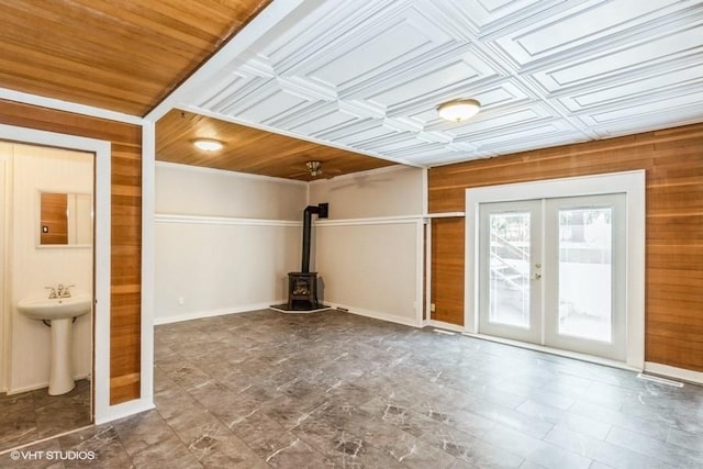 interior space with an ornate ceiling, wood walls, a sink, french doors, and a wood stove