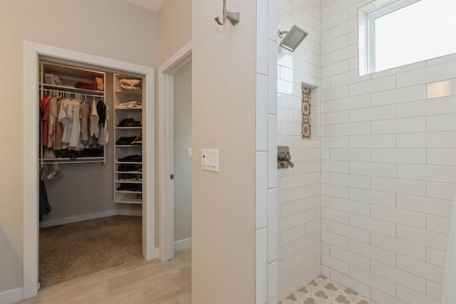 full bath with a spacious closet, baseboards, and a tile shower