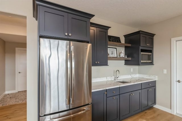 kitchen featuring stainless steel appliances, light wood finished floors, open shelves, and a sink