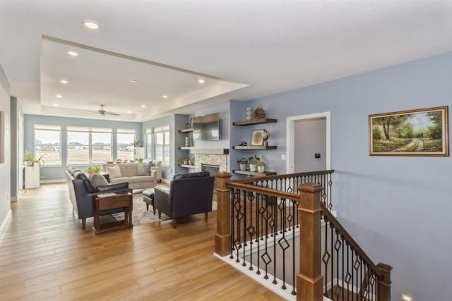 hallway featuring light wood finished floors, a raised ceiling, an upstairs landing, and recessed lighting