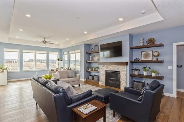 living room with a raised ceiling, a stone fireplace, baseboards, and wood finished floors