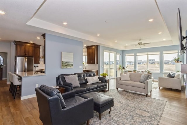 living area with a tray ceiling, wood finished floors, and baseboards