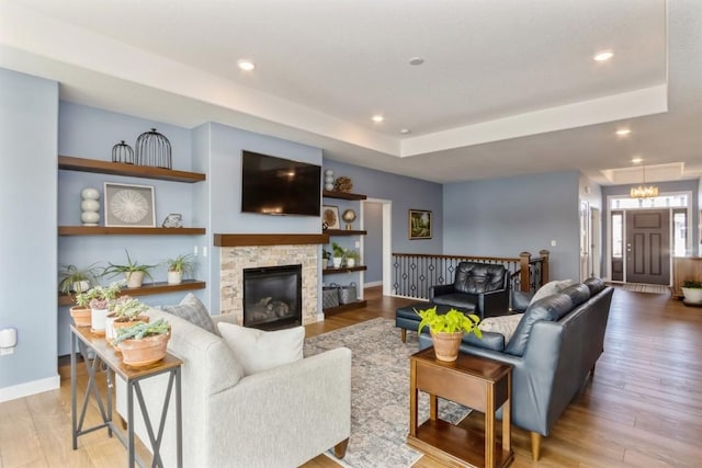 living room with a fireplace, a raised ceiling, light wood-style flooring, and recessed lighting