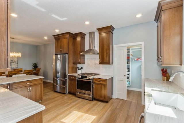 kitchen with appliances with stainless steel finishes, light wood-style floors, a sink, and wall chimney exhaust hood