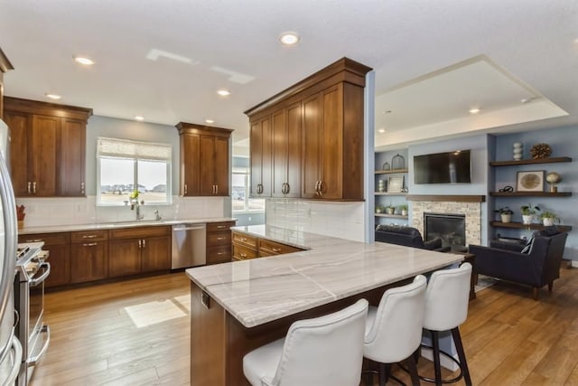 kitchen featuring appliances with stainless steel finishes, a fireplace, light wood-style flooring, and decorative backsplash