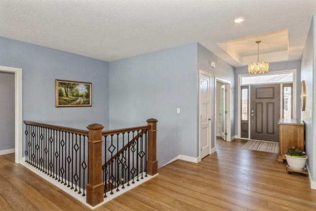 entryway featuring a notable chandelier, baseboards, a raised ceiling, and wood finished floors