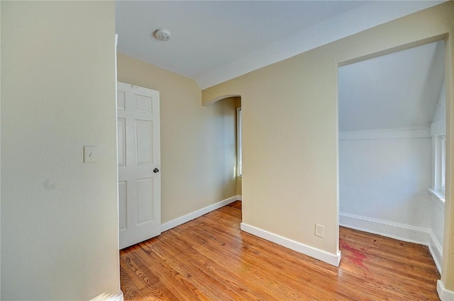 spare room featuring arched walkways, light wood finished floors, and baseboards