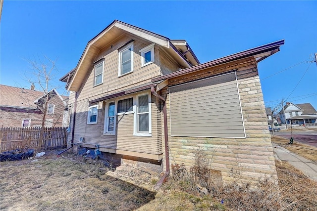 back of house featuring stone siding and fence