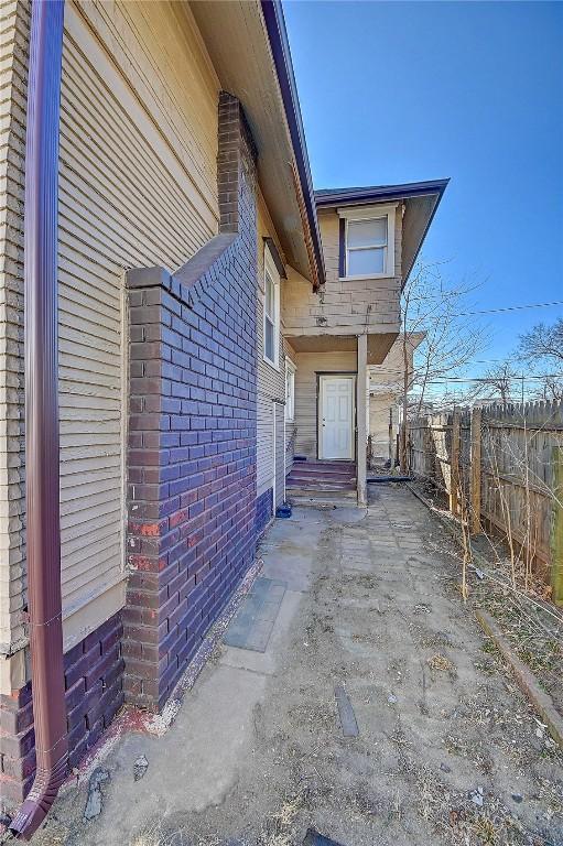 view of property exterior featuring entry steps, brick siding, and fence