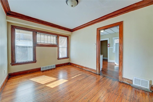 empty room featuring wood-type flooring, visible vents, and crown molding