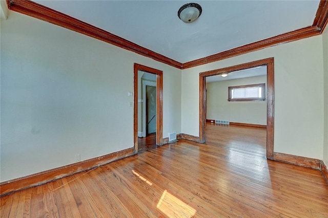 spare room featuring baseboards, light wood-style flooring, visible vents, and crown molding