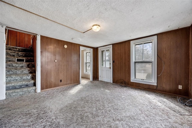 carpeted empty room with a textured ceiling, stairway, and wood walls