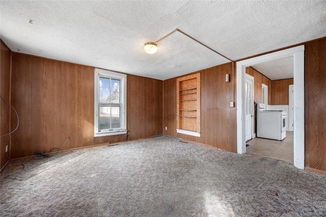 spare room featuring light carpet, wood walls, washer / clothes dryer, and a textured ceiling