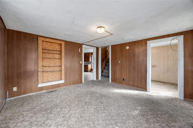 unfurnished room with built in features, carpet, wood walls, a textured ceiling, and stairs