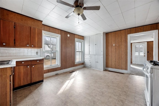 kitchen with wooden walls, light countertops, brown cabinets, light floors, and white gas range