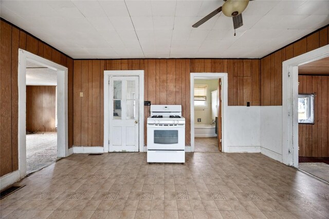 kitchen with wood walls, ceiling fan, white gas range, and brown cabinets