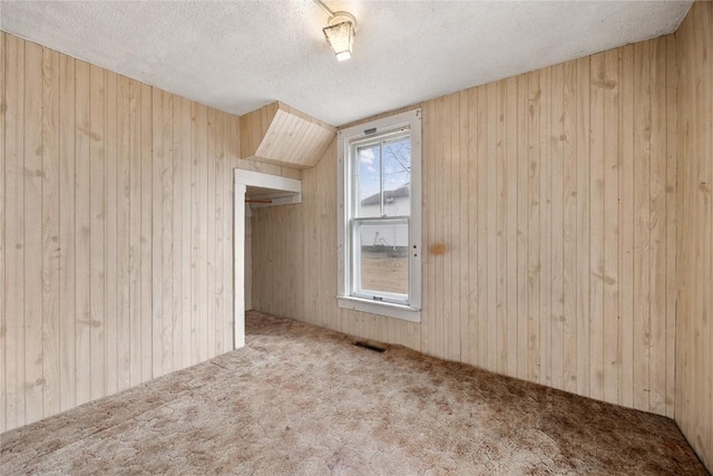 additional living space featuring a textured ceiling, wood walls, carpet, and visible vents