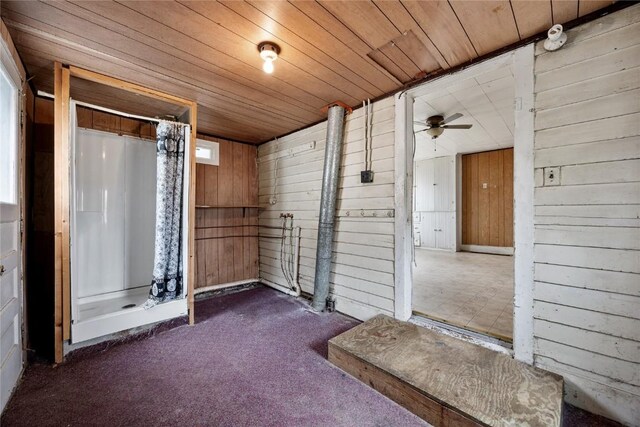 interior space featuring a ceiling fan, a shower with curtain, wood ceiling, and wooden walls