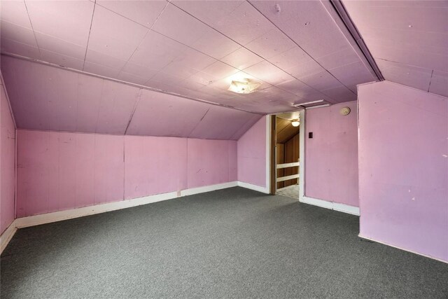 additional living space with lofted ceiling, dark carpet, and baseboards