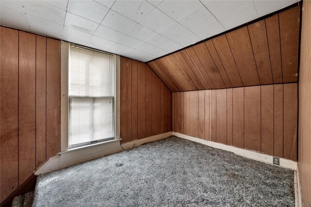 additional living space with vaulted ceiling, carpet flooring, and wooden walls