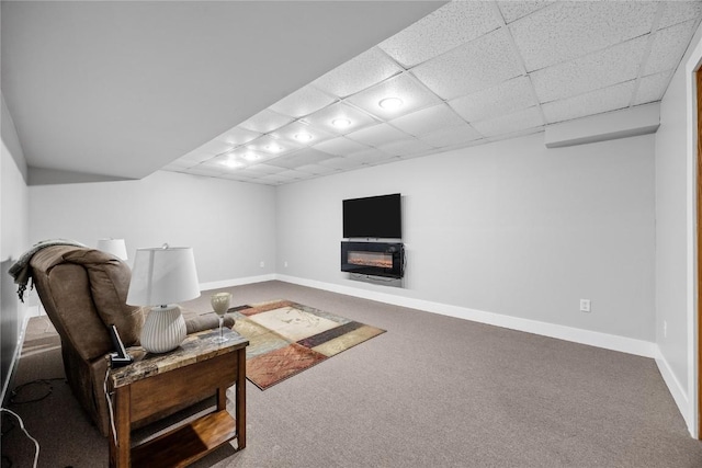 carpeted living area with a glass covered fireplace, a drop ceiling, and baseboards