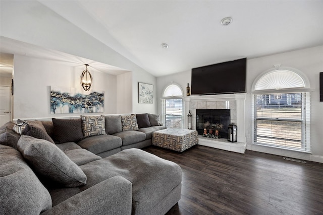 living room featuring a tiled fireplace, visible vents, vaulted ceiling, and dark wood-type flooring