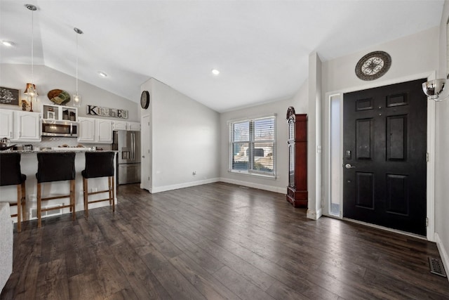 interior space with dark wood finished floors, a breakfast bar area, lofted ceiling, appliances with stainless steel finishes, and white cabinetry